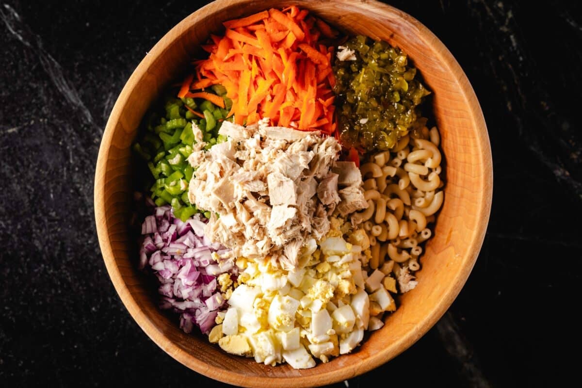 Tuna, macaroni noodles, and chopped veggies in a wooden salad bowl.