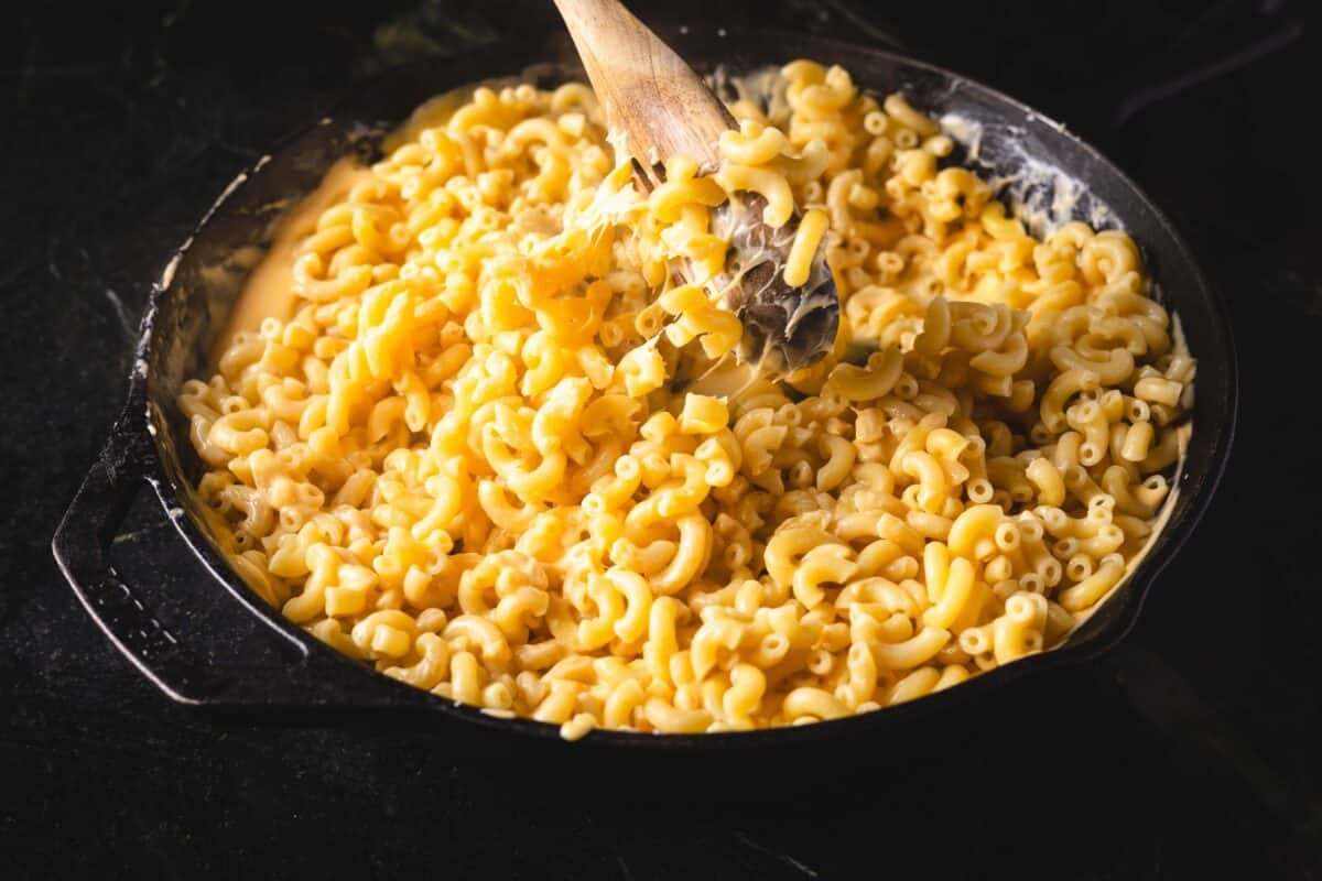 A wooden spoon stirring a skillet of macaroni noodles in sauce.