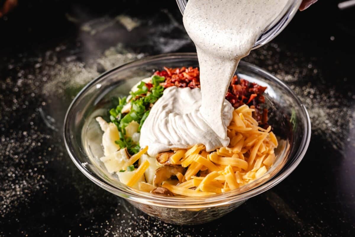 Dressing pouring out of a clear glass bowl into another bowl filled with salad ingredients.