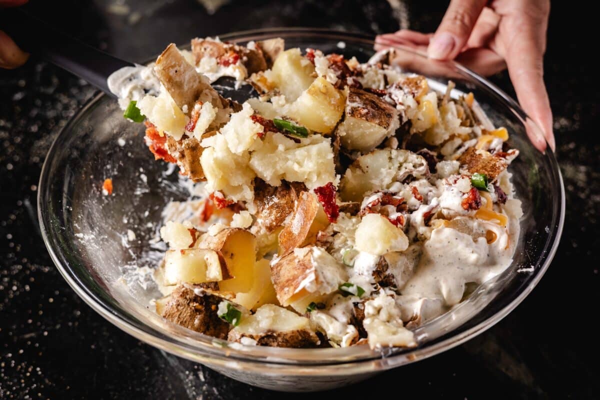 A chef's hands tossing a salad in a clear bowl with a rubber spatula.