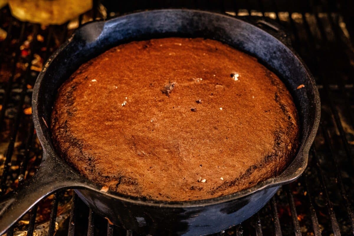 A chocolate cobbler baking in a Dutch oven on the grates of a smoker.