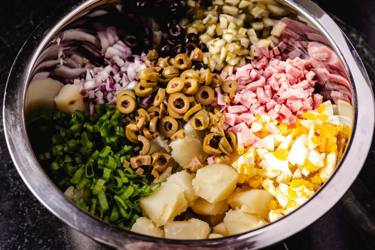 A large bowl full of diced ham, sliced olives, green onions and diced potatoes.