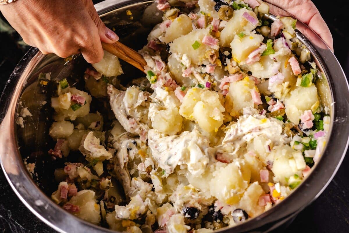 The hand of a chef who uses a wooden spoon to mix a salad in a bowl.