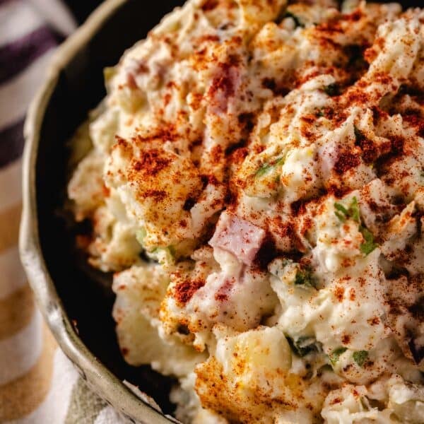 A closeup shot of a bowl filled filled with a hot potato salad, next to a cloth napkin.