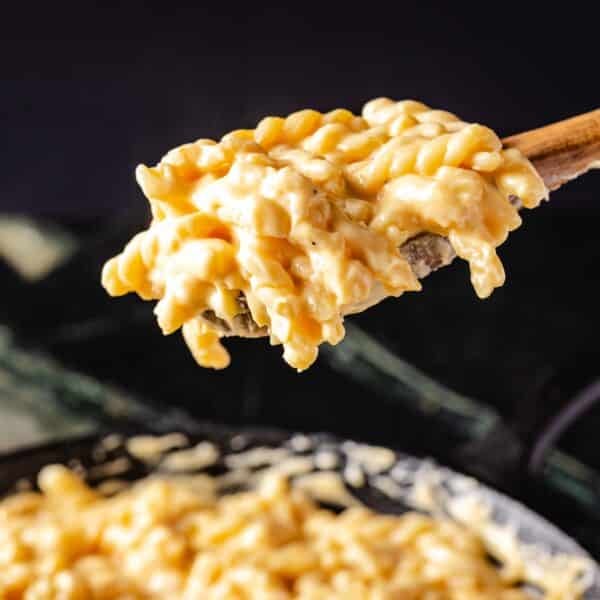 Gemelli pasta on a wooden serving spoon held above a skillet of the dish.