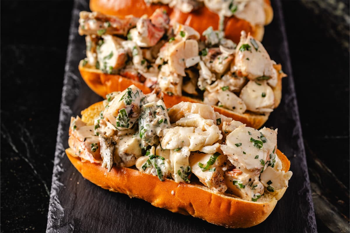 Three lobster rolls stuffed with grilled lobster displayed on a black serving dish.