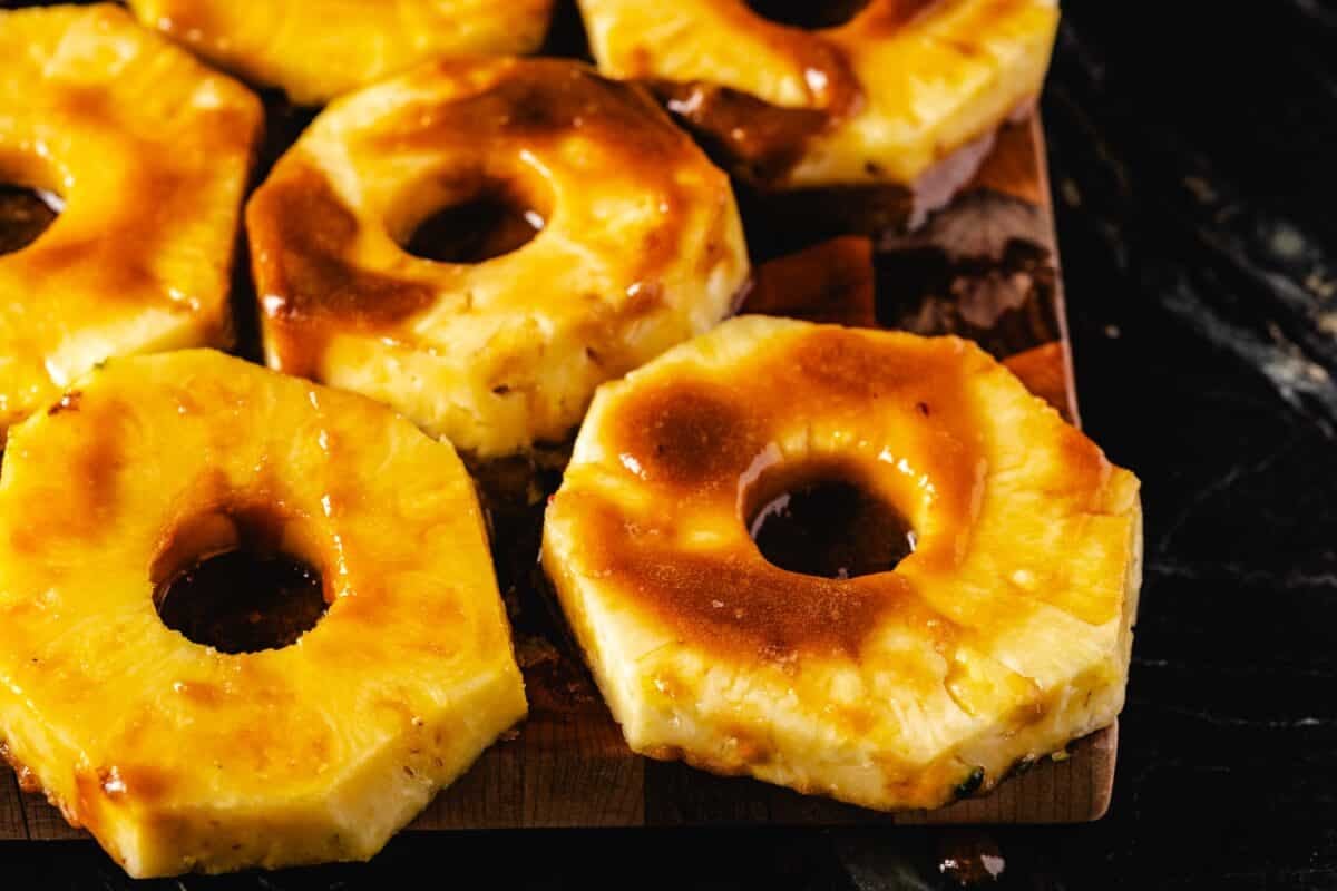 Pineapple rings on a black platter glazed with syrup.