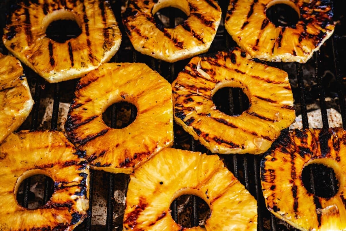 Sliced pineapple rings cooking on the grates of a grill.