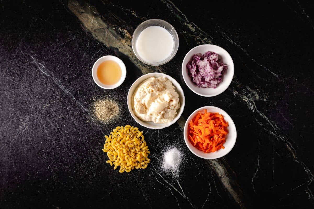 An overhead shot of several bowls and piles of raw ingredients, including uncooked pasta noodles and seasonings.