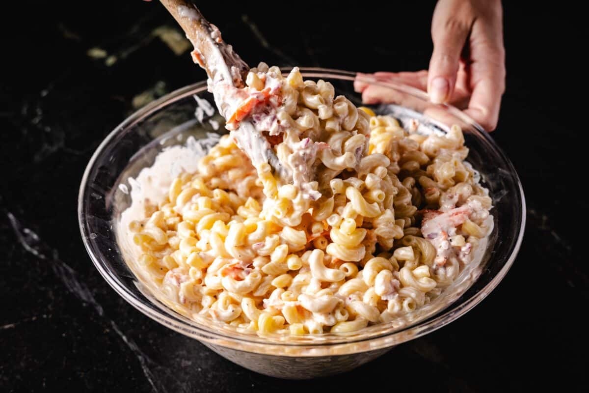 A wooden spoon stirring a cold salad in a glass bowl.