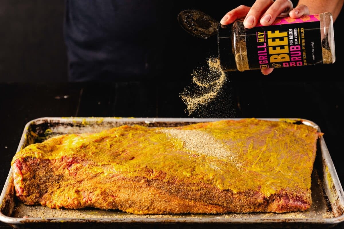 Raw beef on a baking sheet being seasoned with Hey Grill Hey Beef Rub.