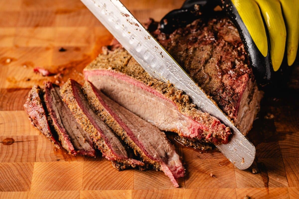 A knife cutting a cooked brisket into slices.