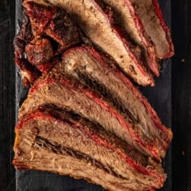 An overhead shot of slices of hot and fast brisket on a black serving platter.