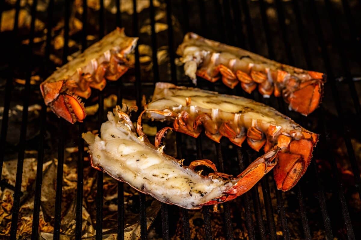 Four lobster tails on the grates of a grill.