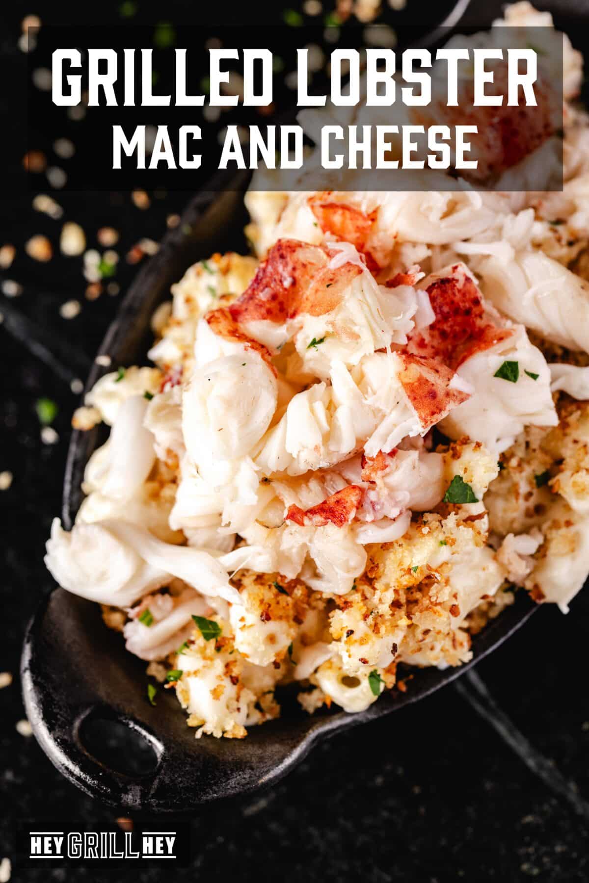 A cast iron dish filled with macaroni topped with lobster chunks. The text overlay reads "Grilled Lobster Mac and Cheese" at the top, and "Hey Grill Hey" at the bottom.