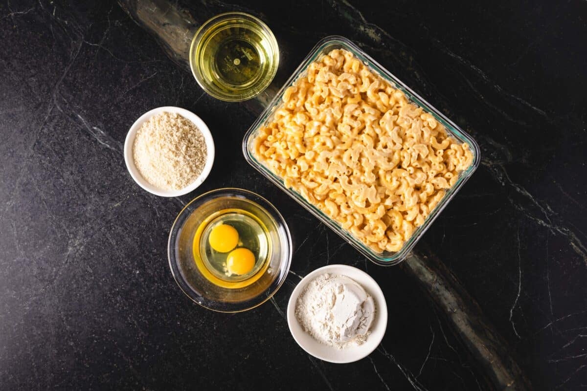 A large baking sheet of macaroni, and 4 small bowls containing olive oil, flour, egg yolks, and bread crumbs.