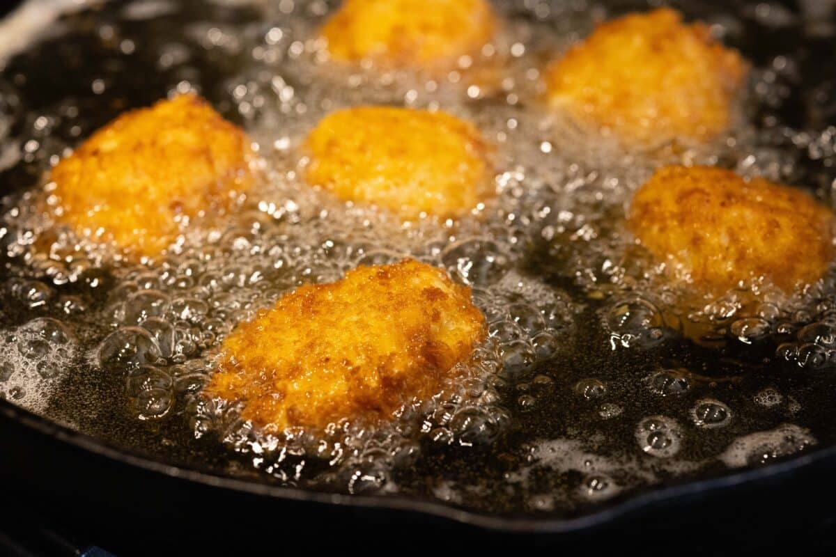 Mac and cheese bites frying in cooking oil.