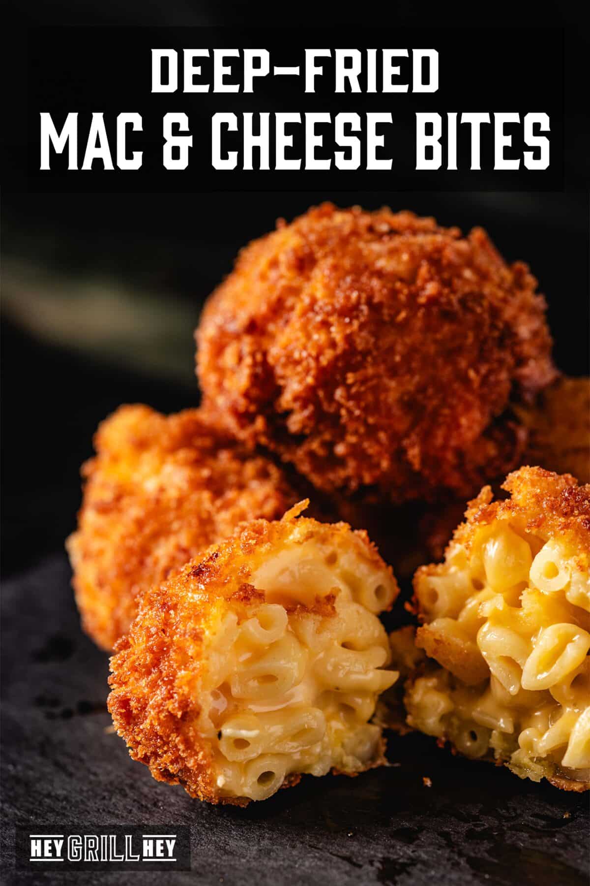 A black platter piled with mac and cheese bites. One is broken open, revealing the creamy mac inside. The text overlay reads "Deep=Fried Mac & Cheese Bites" at the top, and "Hey Grill Hey" at the bottom.