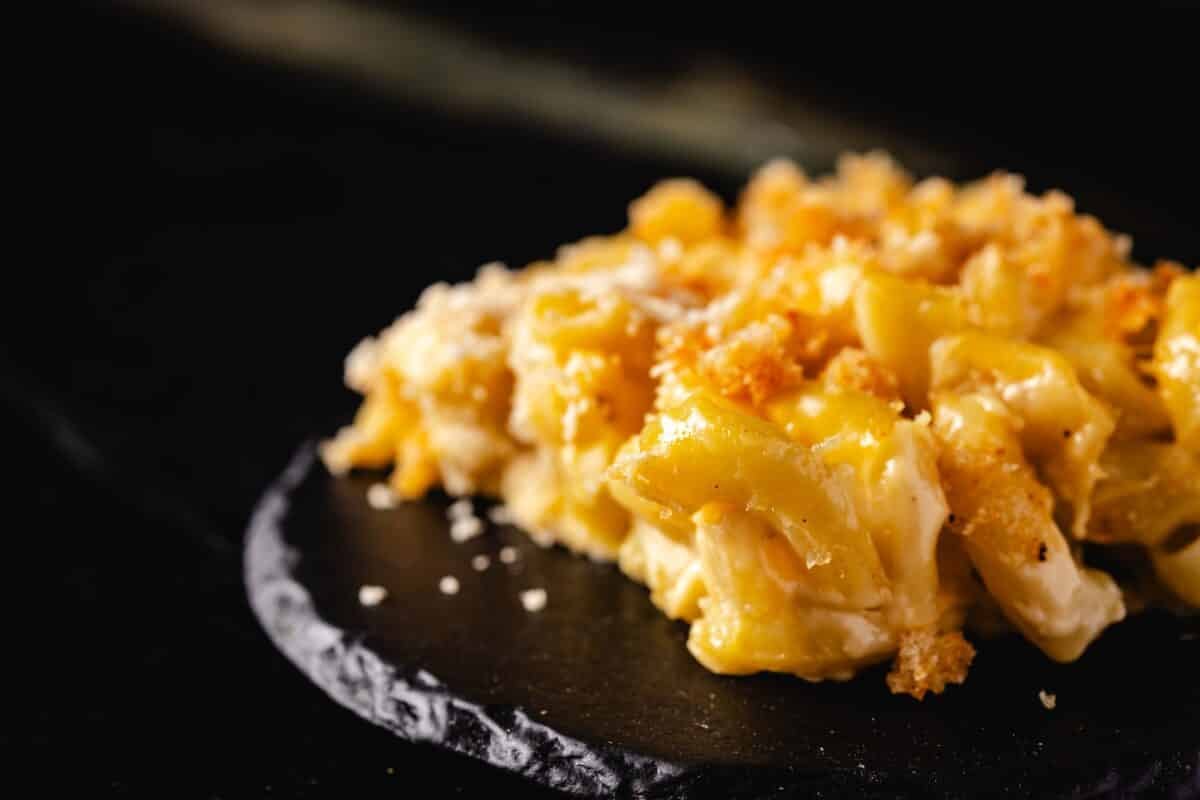 A square of mac and cheese casserole dusted with parmesan, sitting on a round, black platter.