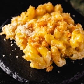 A square of mac and cheese casserole dusted with parmesan, sitting on a round, black platter.