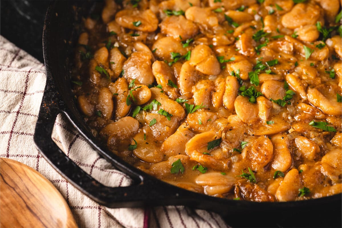 A cast-iron skillet filled with smoky garlic butter beans garnished with parsley and seasoned with Fish & Veggie Rub.