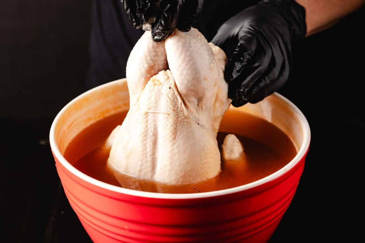 Gloved hands placing raw poultry into a red bowl filled with brown liquid.