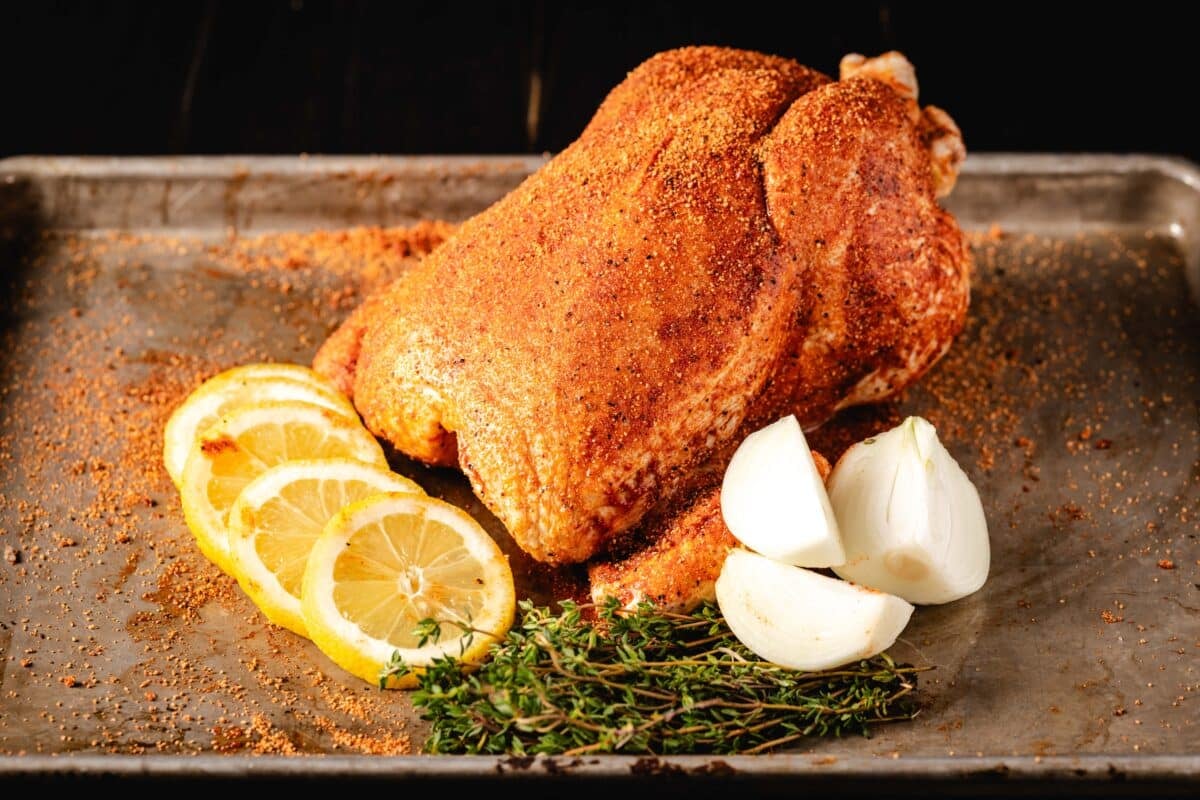 A seasoned bird on a baking sheet with chopped onion, lemon wedges, and sprigs of thyme.