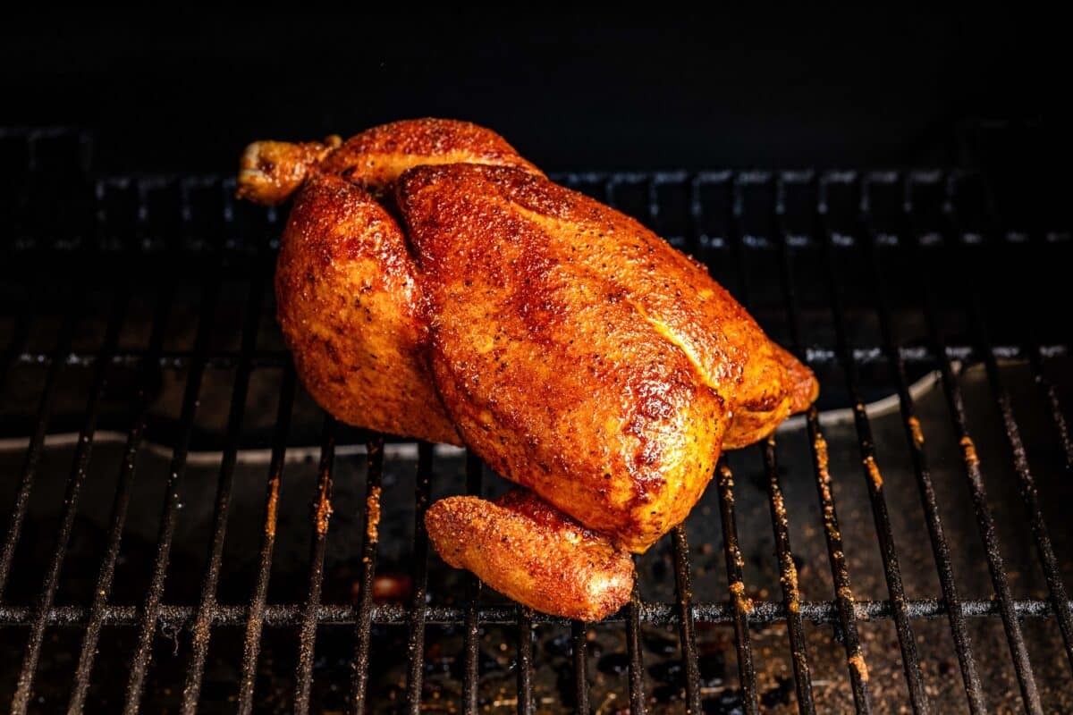 A whole chicken on the grates of a smoker.
