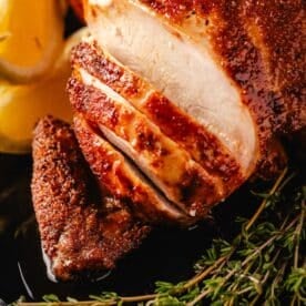 A closeup shot of a sliced smoked chicken on a platter garnished with lemon wedges and sprigs of thyme.
