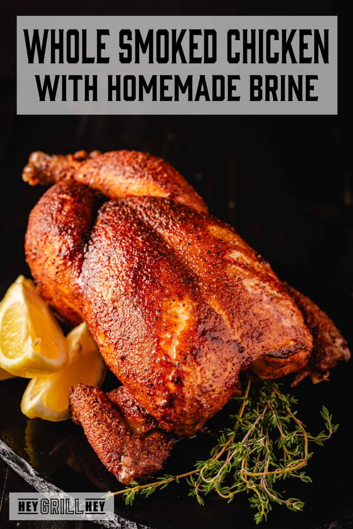 A cooked whole chicken on a platter garnished with lemon wedges and sprigs of thyme. The text overlay reads "Whole Smoked Chicken with Homemade Brine" at the top, and "Hey Grill Hey" at the bottom.