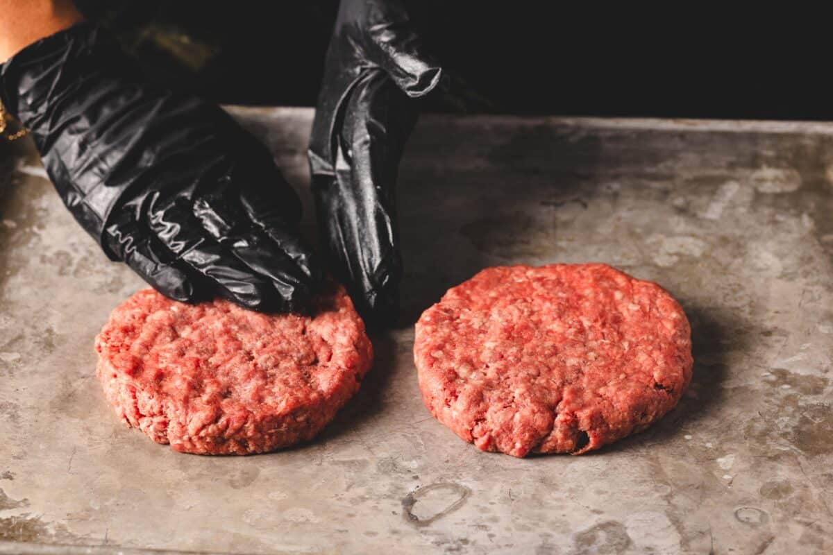A chef's gloved hands forming beef patties on a baking sheet.