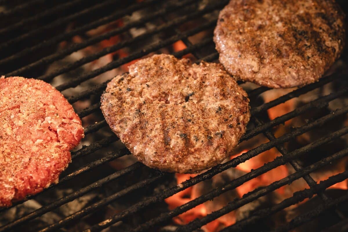 Three burger patties being grilled over charcoal.