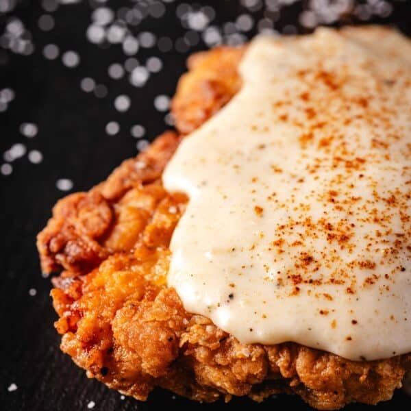 A close up shot of fried chicken cutlet topped with seasoned country gravy.