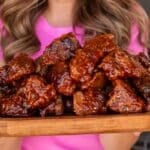 A closeup shot of a wooden platter of battered and sauced brisket cubes.