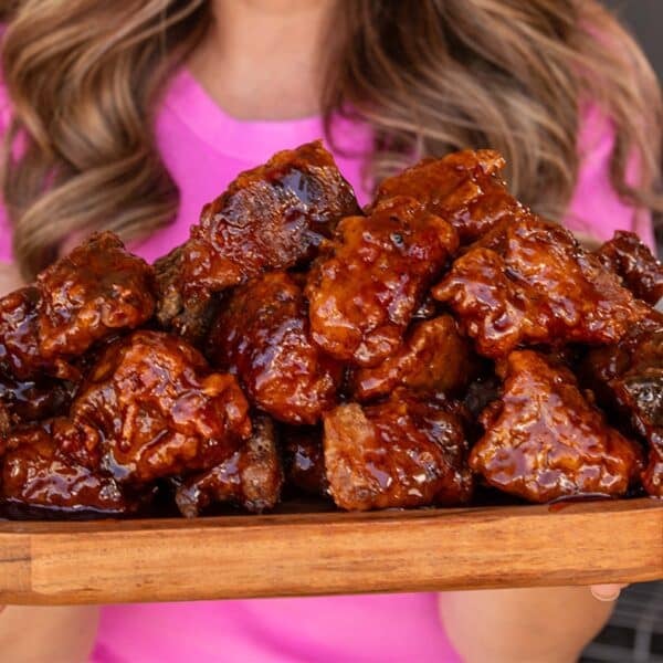 A closeup shot of a wooden platter of battered and sauced brisket cubes.