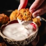 A hand lifting a fried pickle from a dip in a bowl of ranch dressing.