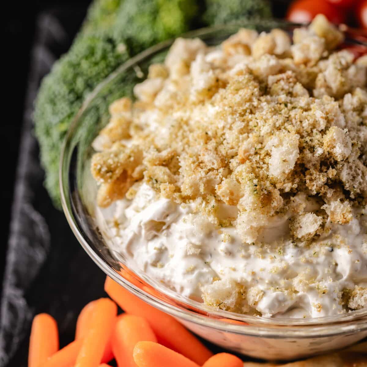 A closeup shot of a bowl of dip next to carrot sticks and broccoli.