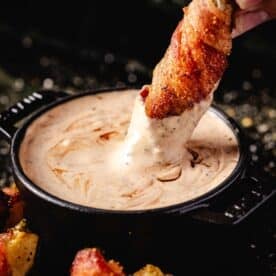A bacon wrapped pickle dipping into a bowl of BBQ ranch dressing.