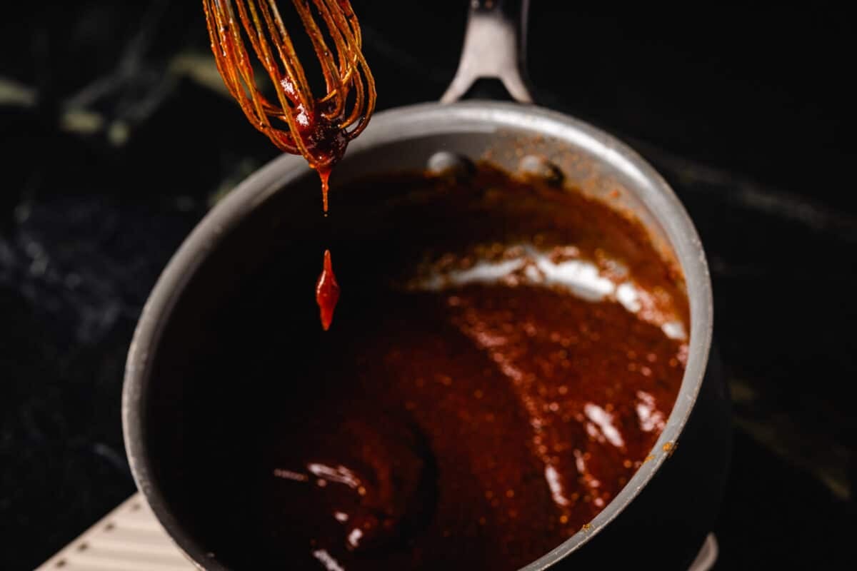 A whisk coated in sauce above a saucepan.