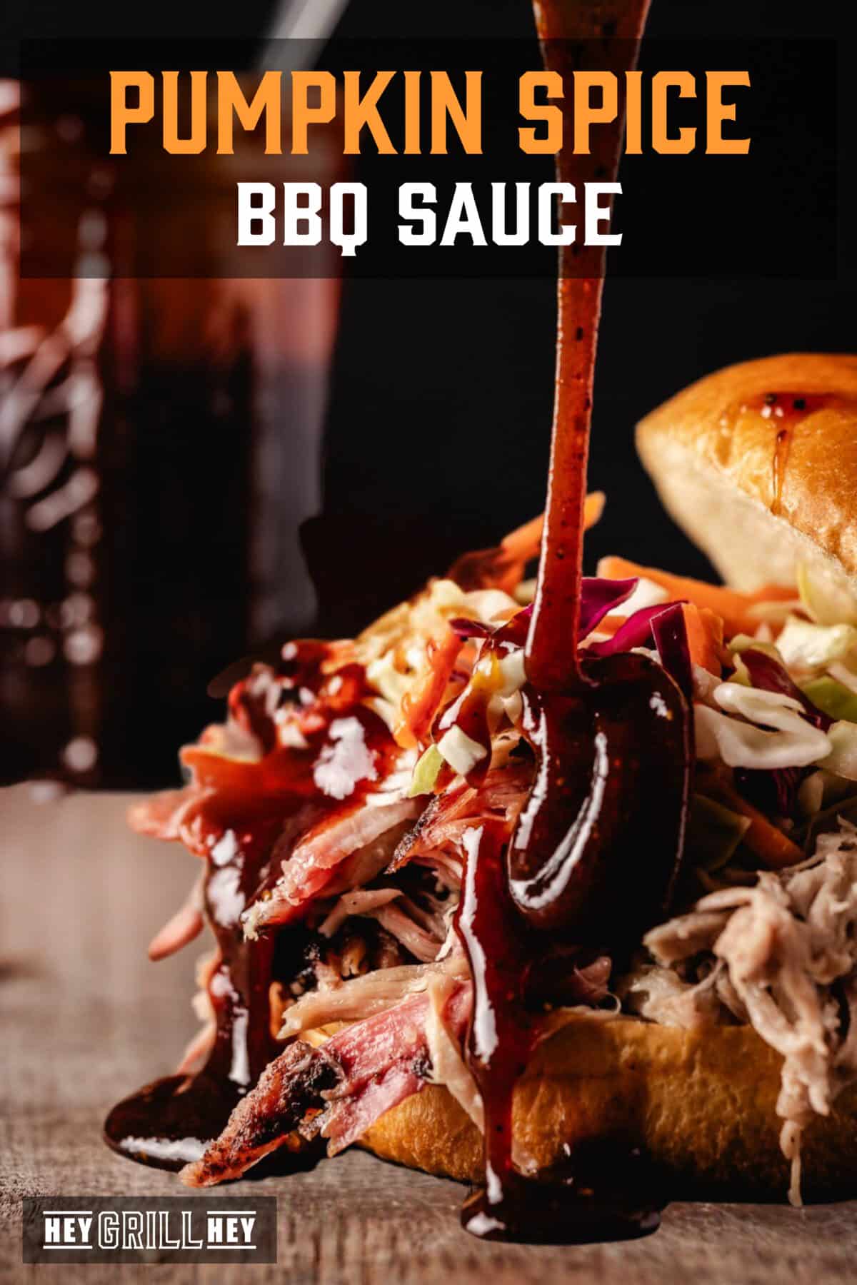 Sauce pouring onto a pulled pork sandwich in front of a jar of the same sauce. The text overlay reads "Pumpkin Spice BBQ Sauce" at the top, and "Hey Grill Hey" at the bottom.