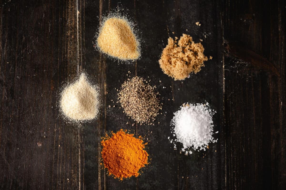 Six small piles of individual spices on a wooden surface.