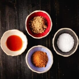 An overhead shot of four bowls containing (clockwise from top) brown sugar, salt, BBQ rub, and hot sauce.