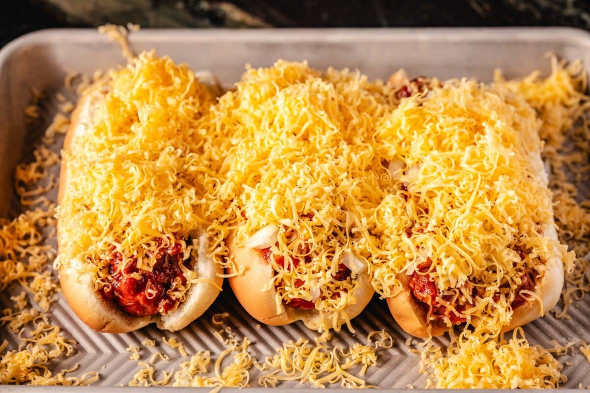 A pan flanked by hot dogs on sandwiches seasoned with grated keddar.