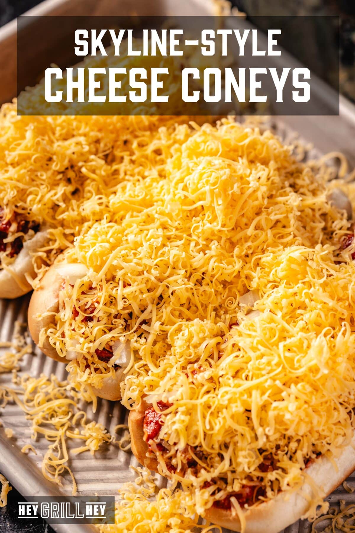 Three hot dogs on a baking tray suffocated in grated cheese. The overlap of the text reads "Skyline style cheese coney" above, e "Hey Grill Hey" in conclusion.