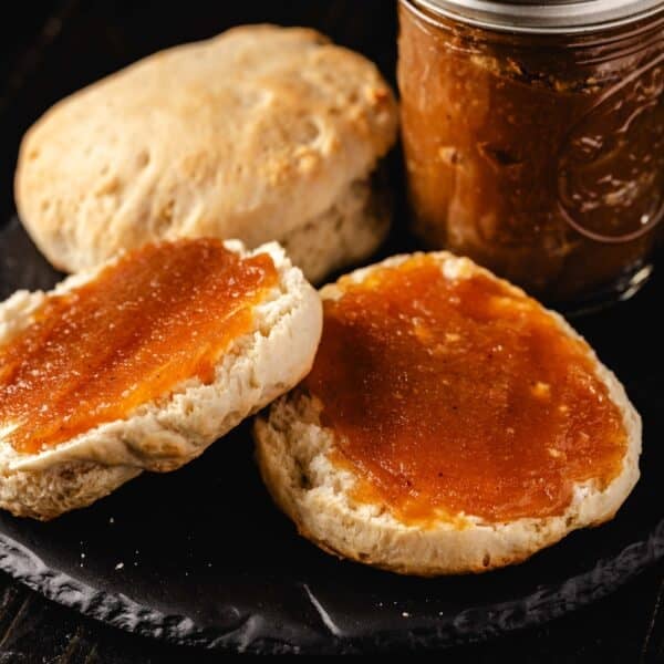 A biscuit with jam, a dry biscuit, and a jar of jam, all on a black plate.