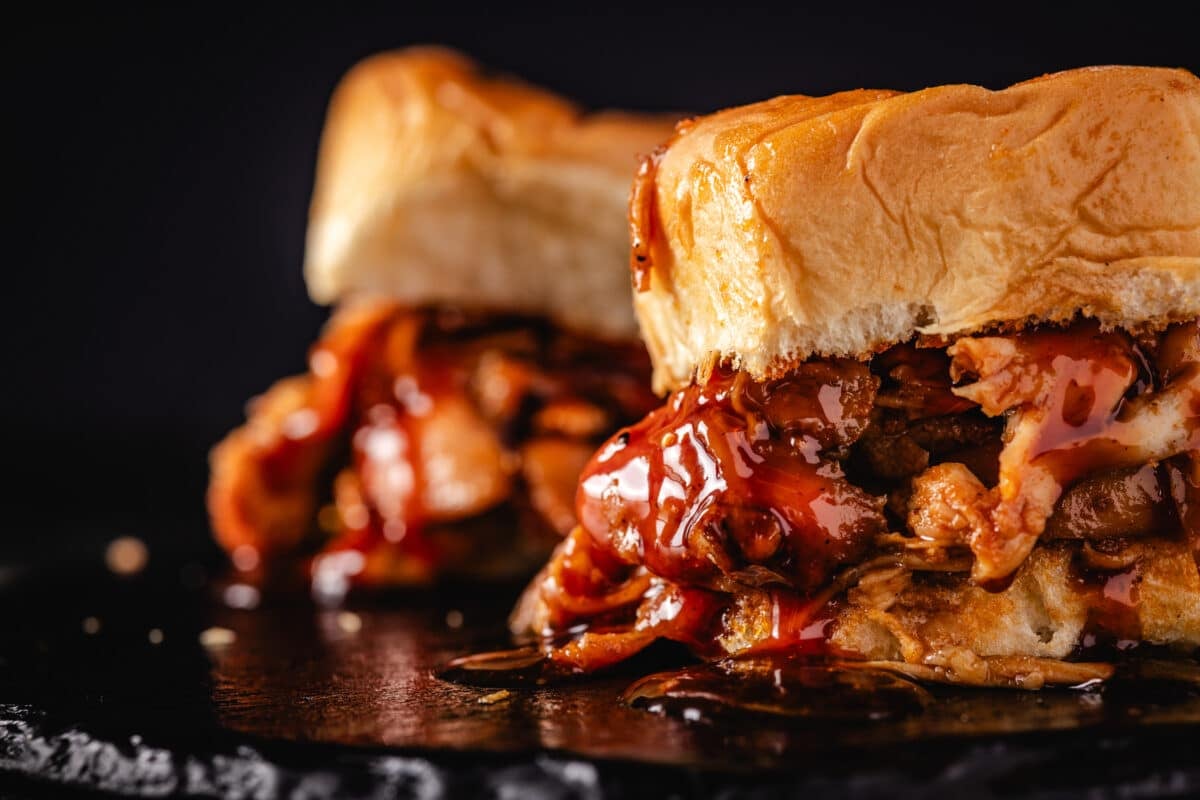 A closeup shot of 2 BBQ chicken sliders dripping with sauce.