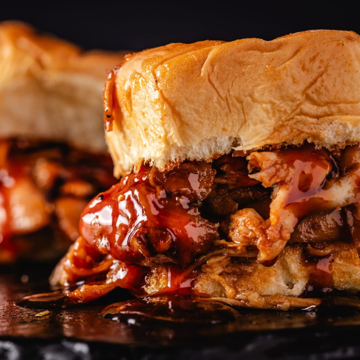 A closeup shot of a shredded chicken sandwich dripping with BBQ sauce.