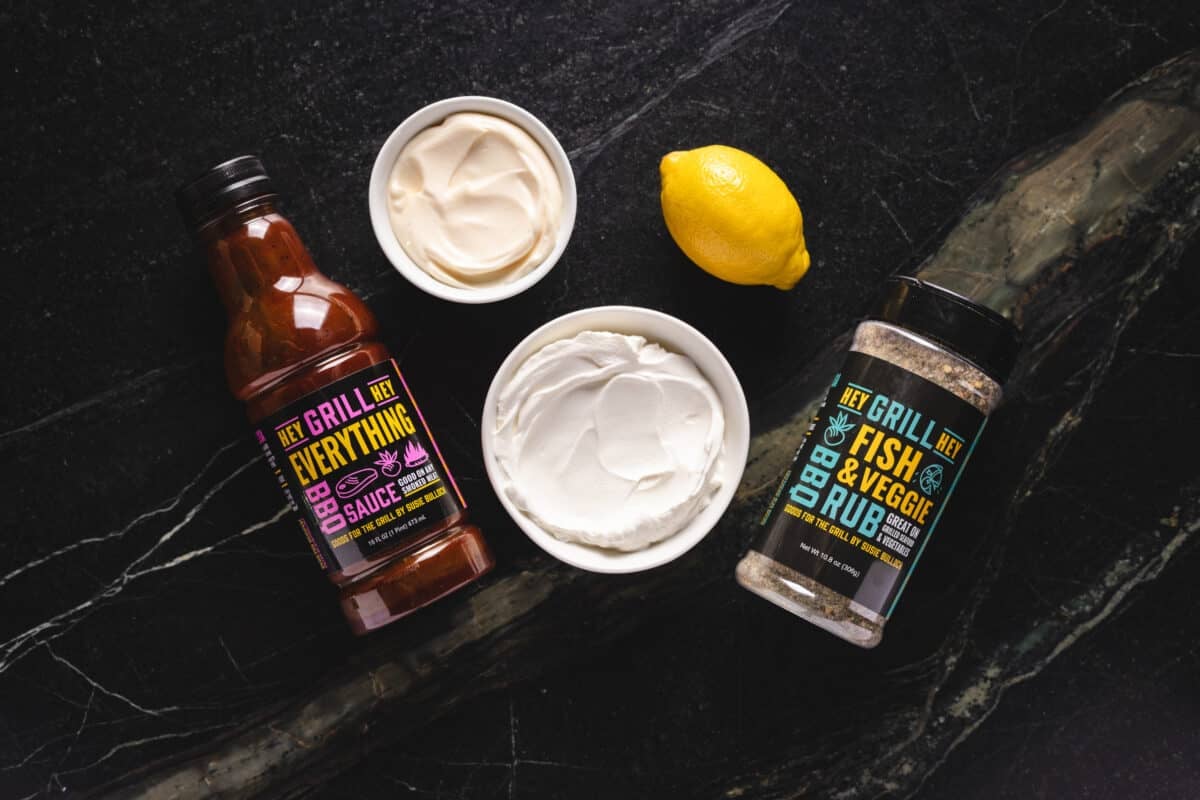 An overhead shot of a lemon, bowls of sour cream and mayo, and bottles of Hey Grill Hey Everything Sauce and Fish & Veggie Rub.