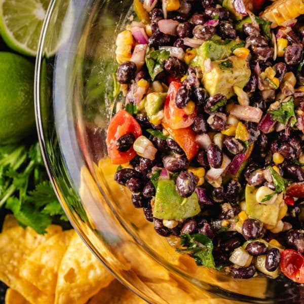 An overhead shot of a bowl of black bean salad next to chips and lime wedges.