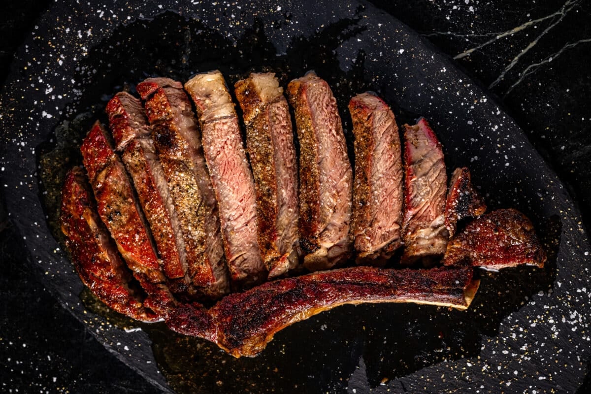 Steak slices shingled on a black plate next to the bone.